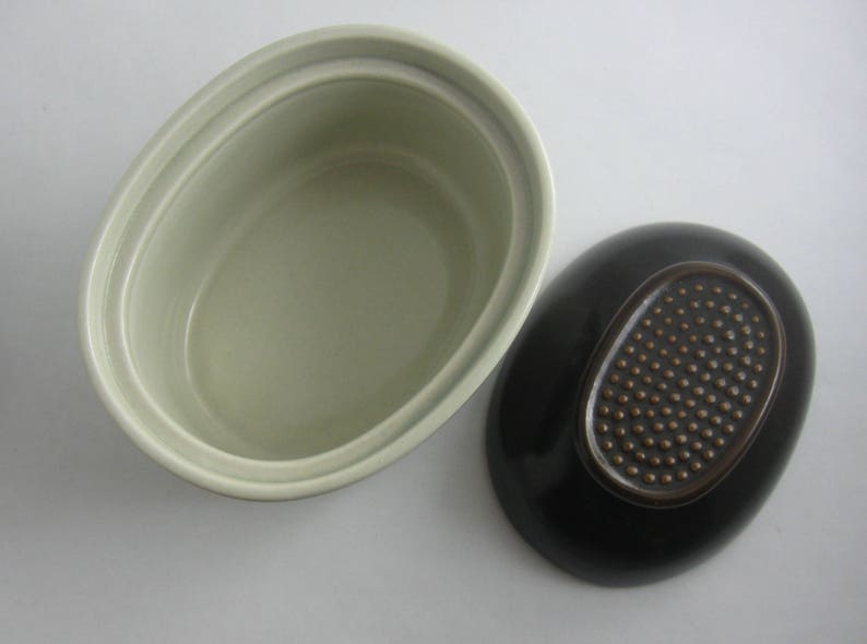 May include: A set of two oval ceramic dishes. One dish is light green with a smooth finish. The other dish is black with a brown oval design.