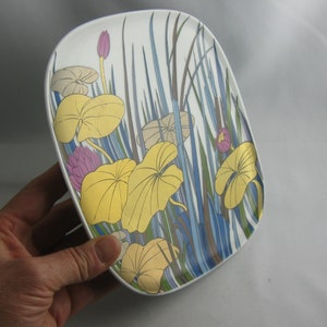 May include: A white ceramic plate with a floral design featuring yellow, blue, green, and pink flowers. The plate has a rounded rectangular shape.