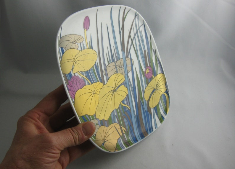 May include: A white ceramic plate with a floral design featuring yellow, blue, green, and pink flowers. The plate has a rounded rectangular shape.