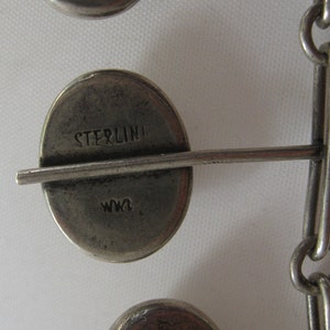 May include: Close-up of a silver chain bracelet with a round charm that says "STERLING" and "W.K."