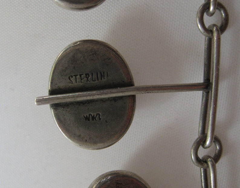 May include: Close-up of a silver chain bracelet with a round charm that says "STERLING" and "W.K."