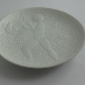 May include: White porcelain plate with a raised design of a figure with a peacock and floral motifs.