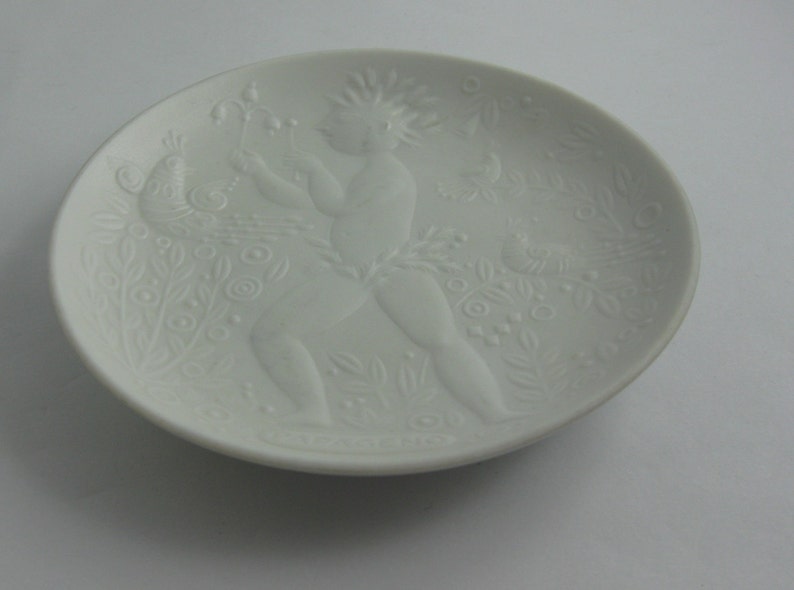 May include: White porcelain plate with a raised design of a figure with a peacock and floral motifs.