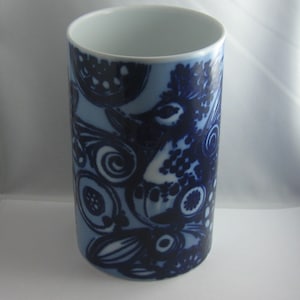 May include: A white ceramic cylinder vase with a blue and white abstract pattern. The pattern features stylized birds and swirls.