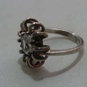 May include: A silver ring with a clear stone set in a flower-shaped design.