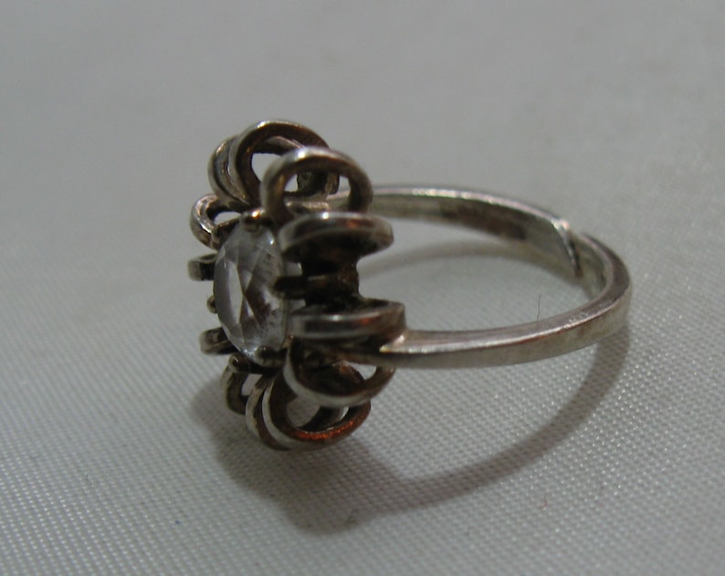May include: A silver ring with a clear stone set in a flower-shaped design.