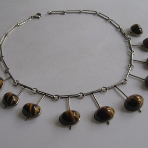 May include: A silver necklace with a chain and nine brown and gold tiger's eye stones hanging from it.