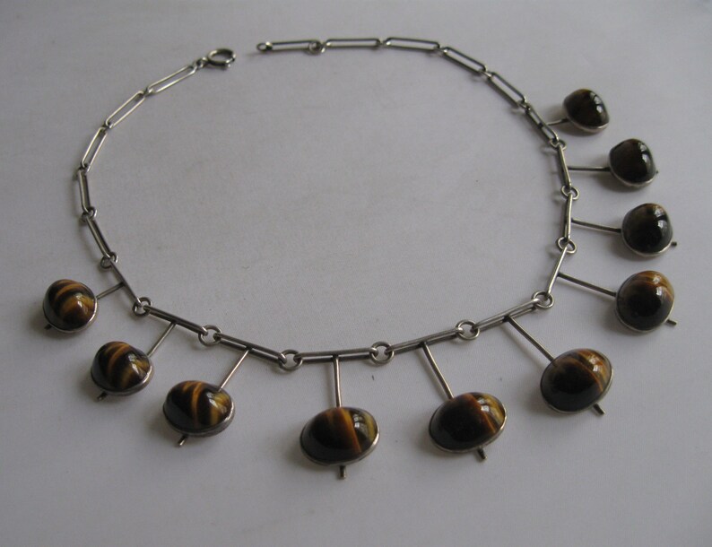 May include: A silver necklace with a chain and nine brown and gold tiger's eye stones hanging from it.