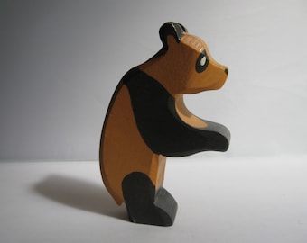 Puede incluir: Un oso panda de juguete de madera pintado de negro y marrón. El panda está de pie sobre sus patas traseras con las patas delanteras levantadas.