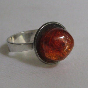 Könnte beinhalten: Ein Silberring mit einem großen, runden Bernstein, der in einer Zargenfassung gefasst ist.