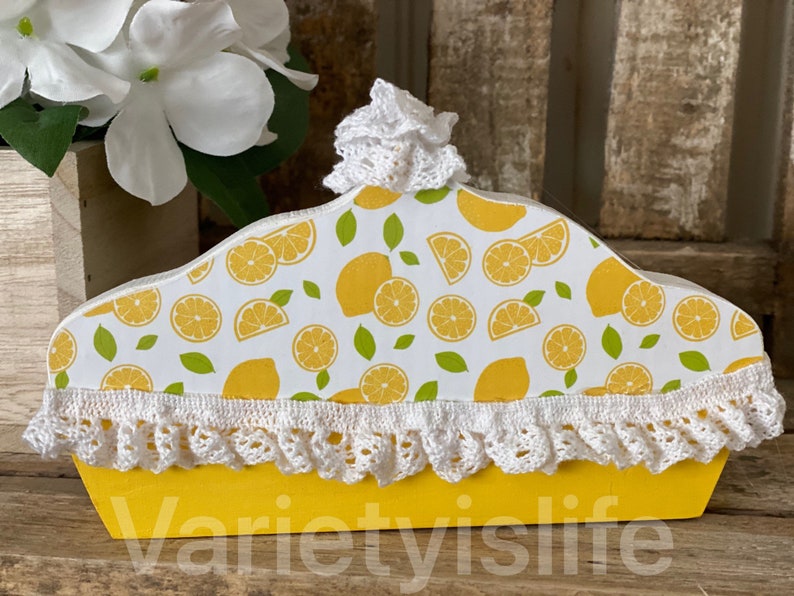 May include: A yellow wooden box with a lemon print and white crocheted trim. The box is shaped like a pie crust and has the text "varietyislife" on the bottom.