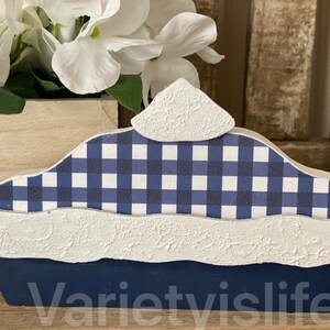 May include: A blue and white checkered pie crust with a white, textured top. The pie crust is made of wood and is a decorative piece.