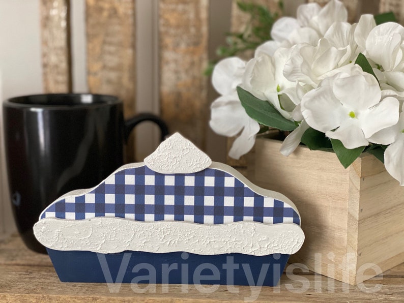 May include: A blue and white checkered pie with a white crust and a blue base. The pie is made of wood and is a decorative piece.