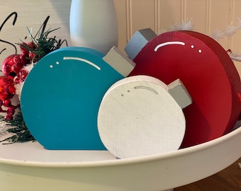 May include: Three wooden Christmas ornaments in a tiered tray. The ornaments are painted in red, white, and teal blue. Each ornament has a white dot design.