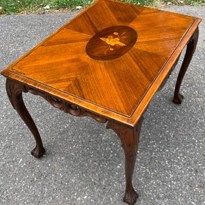 May include: A rectangular wooden side table featuring a polished brown finish with a prominent central oval inlay depicting a yellow floral design. The table has four curved legs with carved detailing and claw-style feet at the base.