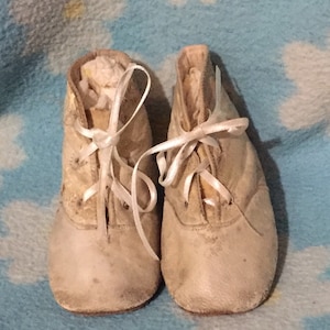 May include: A pair of white leather baby shoes with white laces. The shoes are worn and have a vintage look.