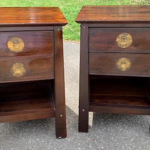 May include: A pair of dark brown wooden nightstands, each featuring two drawers with circular brass hardware and a lower open shelf. The furniture pieces have a rectangular top surface and four sturdy legs, showcasing a visible wood grain finish.
