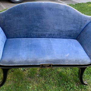 May include: A blue velvet settee featuring a curved backrest, rolled arms, and a dark wood frame with carved detailing. The upholstery is a solid light blue fabric, and the base is supported by four curved legs with a dark finish and gold accents.