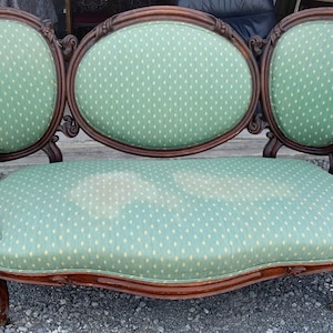 May include: A vintage, three-seater sofa with a green fabric upholstery featuring a small, white diamond pattern. The sofa has a carved wooden frame with ornate details and curved arms.
