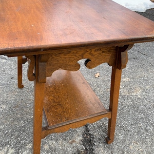 May include: A vintage wooden side table with a rectangular top and a lower shelf. The table is made of a warm-toned wood, with decorative carved details on the apron and legs. The table measures approximately 30 inches long, 18 inches wide, and 28 inches high.