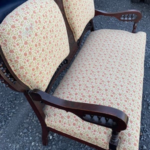 May include: A vintage wooden settee with a floral patterned fabric upholstery. The settee has a dark brown finish and intricate carvings on the arms and legs.