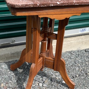 May include: A small, antique side table with a rectangular top made of reddish-brown marble. The table's wooden frame is a warm brown color, featuring carved details and curved legs. This vintage table is a decorative accent piece.