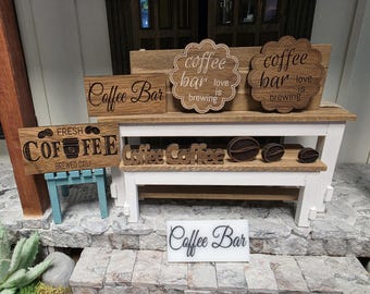 May include: A collection of wooden coffee-themed decor items including rectangular signs with the text Coffee Bar and Fresh Coffee Brewed Daily, two scalloped signs reading coffee bar love is brewing, cutout coffee words, and three coffee bean shapes.