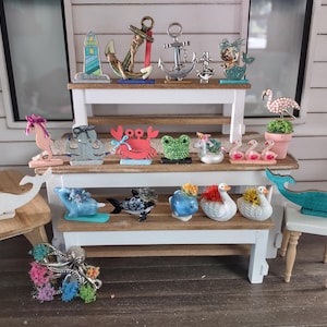 Puede incluir: Una colección de objetos decorativos con temática náutica y animal, que incluye anclas, una sirena, un caballito de mar, un cangrejo, una rana, cisnes y ballenas. Los artículos se exhiben en pequeñas mesas de madera.