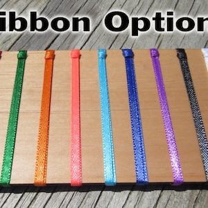 Pode incluir: Close-up de uma placa de madeira com nove op&ccedil;&otilde;es de fita de diferentes cores. As cores s&atilde;o vermelho, verde, laranja, rosa, azul, azul escuro, roxo, preto e branco.
