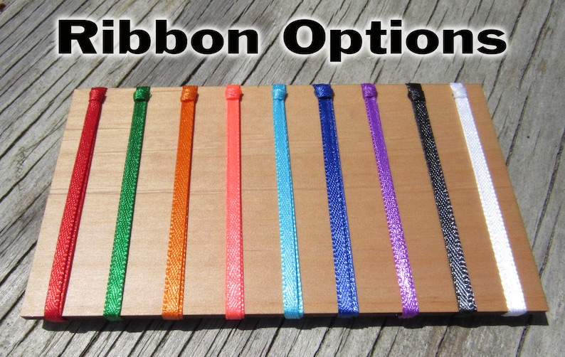 Pode incluir: Close-up de uma placa de madeira com nove op&ccedil;&otilde;es de fita de diferentes cores. As cores s&atilde;o vermelho, verde, laranja, rosa, azul, azul escuro, roxo, preto e branco.
