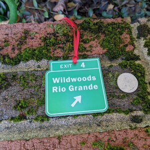May include: Green and white exit sign with the text "Exit 4 Wildwoods Rio Grande" and an arrow pointing to the right. The sign is attached to a red ribbon.
