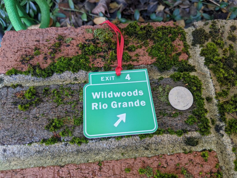 May include: Green and white exit sign with the text "Exit 4 Wildwoods Rio Grande" and an arrow pointing to the right. The sign is attached to a red ribbon.
