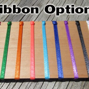 May include: A selection of ribbon colors, including red, green, orange, pink, blue, purple, black, and white, displayed on a wooden surface.  Ribbon Options.