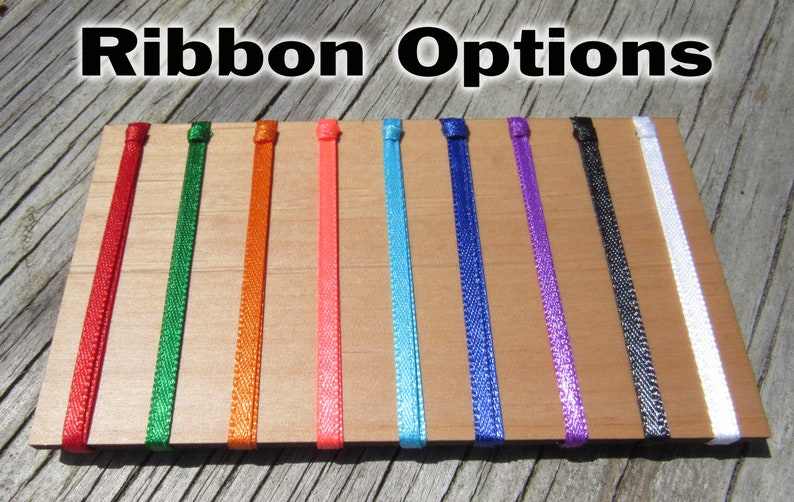 May include: A selection of ribbon colors, including red, green, orange, pink, blue, purple, black, and white, displayed on a wooden surface.  Ribbon Options.