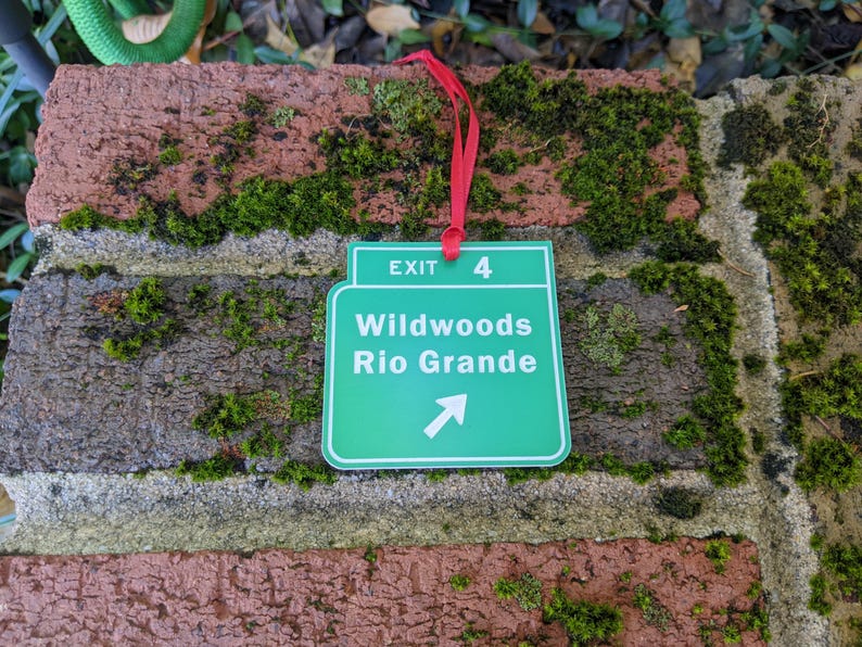 May include: Green exit sign with white text that reads "Exit 4 Wildwoods Rio Grande" with a white arrow pointing to the right. The sign is hanging from a red ribbon.