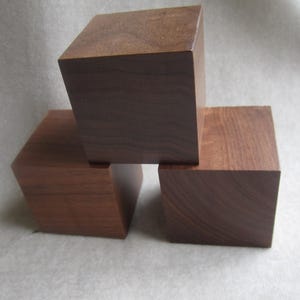 May include: Three wooden blocks stacked on top of each other. The blocks are made of dark brown wood and have a smooth, polished finish.