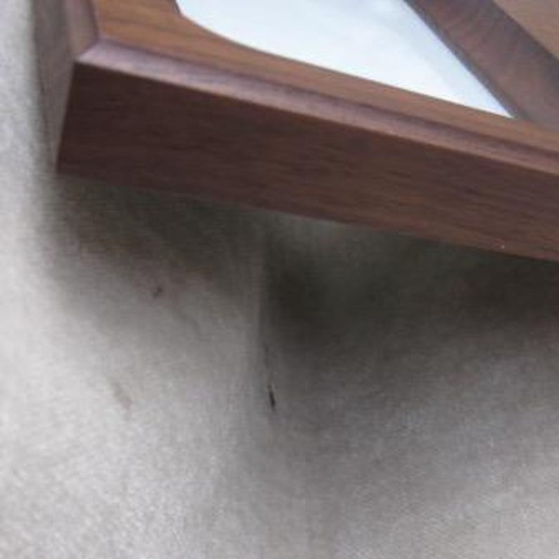 May include: A rectangular picture frame constructed from dark brown wood with a visible natural grain pattern. The frame features a clean, angled edge profile and surrounds a white interior space, showcasing a simple and functional design.