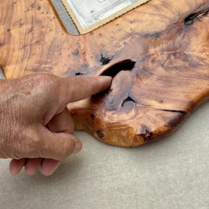 May include: A polished wooden picture frame crafted from a natural slab with a prominent live edge and visible wood grain. The frame features a dark, irregular knot hole in the center of the wood surface and holds a vintage black and white photograph.