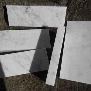 May include: A collection of white marble tiles with gray veining. The tiles are rectangular and square, with some having angled edges. The arrangement suggests a potential for use in home decor or construction projects.