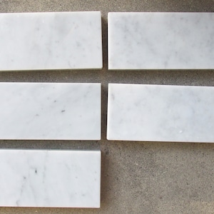 May include: Five white marble tiles arranged in a grid pattern. The tiles are rectangular and have a smooth, polished surface.