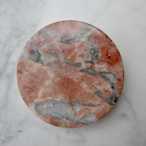 May include: A round, pink and gray marble coaster with a swirling pattern.