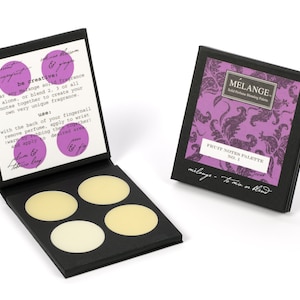 May include: A black box with four round, pale yellow scented wax discs. The box is open and the inside lid has instructions for using the wax discs. The text on the lid reads "be creative: wear any Melange solid fragrance alone, or blend 2, 3 or all notes together to create your own very unique fragrance. use: with the back of your fingernail remove perfume, apply to wrist (warm by rubbing them together!) and apply to desired area. palm &  &  tobacco leaf"