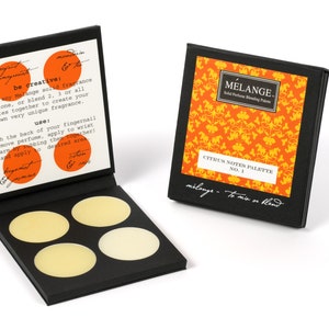 May include: A black box with four round, yellow-colored solid perfume samples. The box is open and the lid has instructions for using the perfume. The box is labeled "MELANGE. Solid Perfume Blending Palette" and "CITRUS NOTES PALETTE NO. 1".