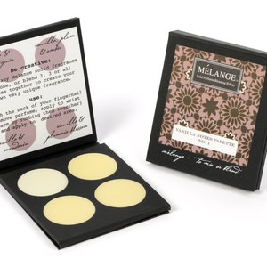 May include: A black box with four round, white, solid perfume discs. The box is open and the lid has instructions for using the perfume. The text on the lid reads "be creative: wear any Melange solid fragrance alone, or blend 2, 3 or all notes together to create your own very unique fragrance. use: with the back of your fingernail remove perfume, apply to wrist (warm by rubbing them together) and apply to desired area."