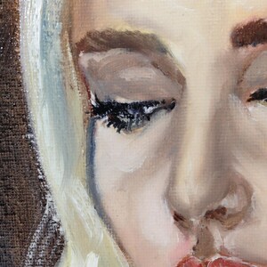 May include: A close-up of a woman's face with blonde hair. Her eyes are closed and she has a tear running down her cheek. Her lips are slightly parted and her expression is sad.
