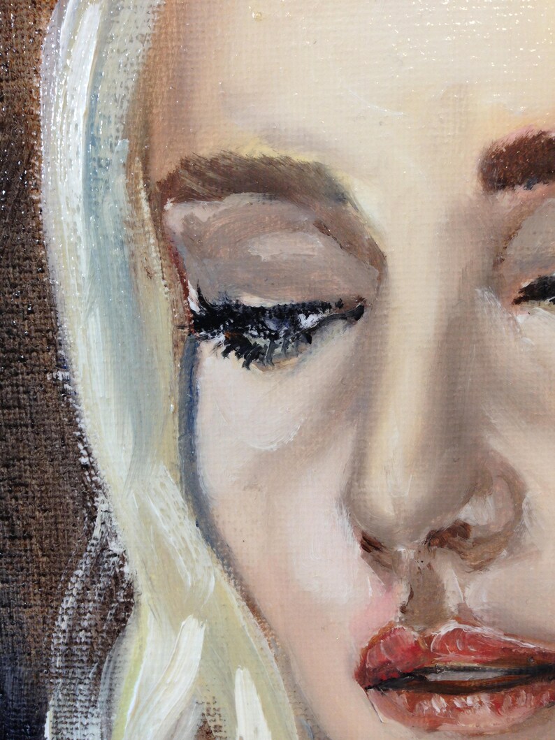 May include: A close-up of a woman's face with blonde hair. Her eyes are closed and she has a tear running down her cheek. Her lips are slightly parted and her expression is sad.