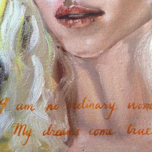 May include: A painting of a woman with blonde hair and red lips. The text "I am no ordinary woman. My dreams come true." is written in orange paint on the woman's chest.