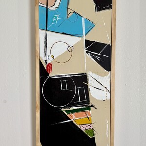 May include: Abstract art painting in a rectangular wooden frame. The artwork features geometric shapes in black, beige, blue, white, and pink. A large black circle with white lines and the number 9 in blue are visible.