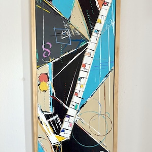 May include: Abstract art painting in a rectangular wooden frame. The artwork features geometric shapes in black, blue, beige, and orange, with colorful accents. The composition includes lines, circles, and a grid-like structure.