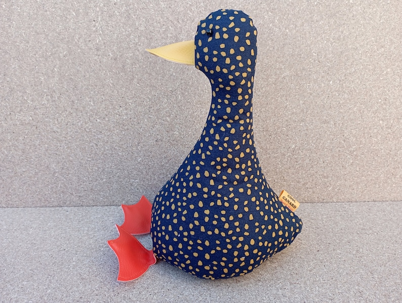 May include: A blue and gold polka dot fabric duck doorstop with red fabric feet. The duck has a yellow beak and a small tag that says "Cool Canard".
